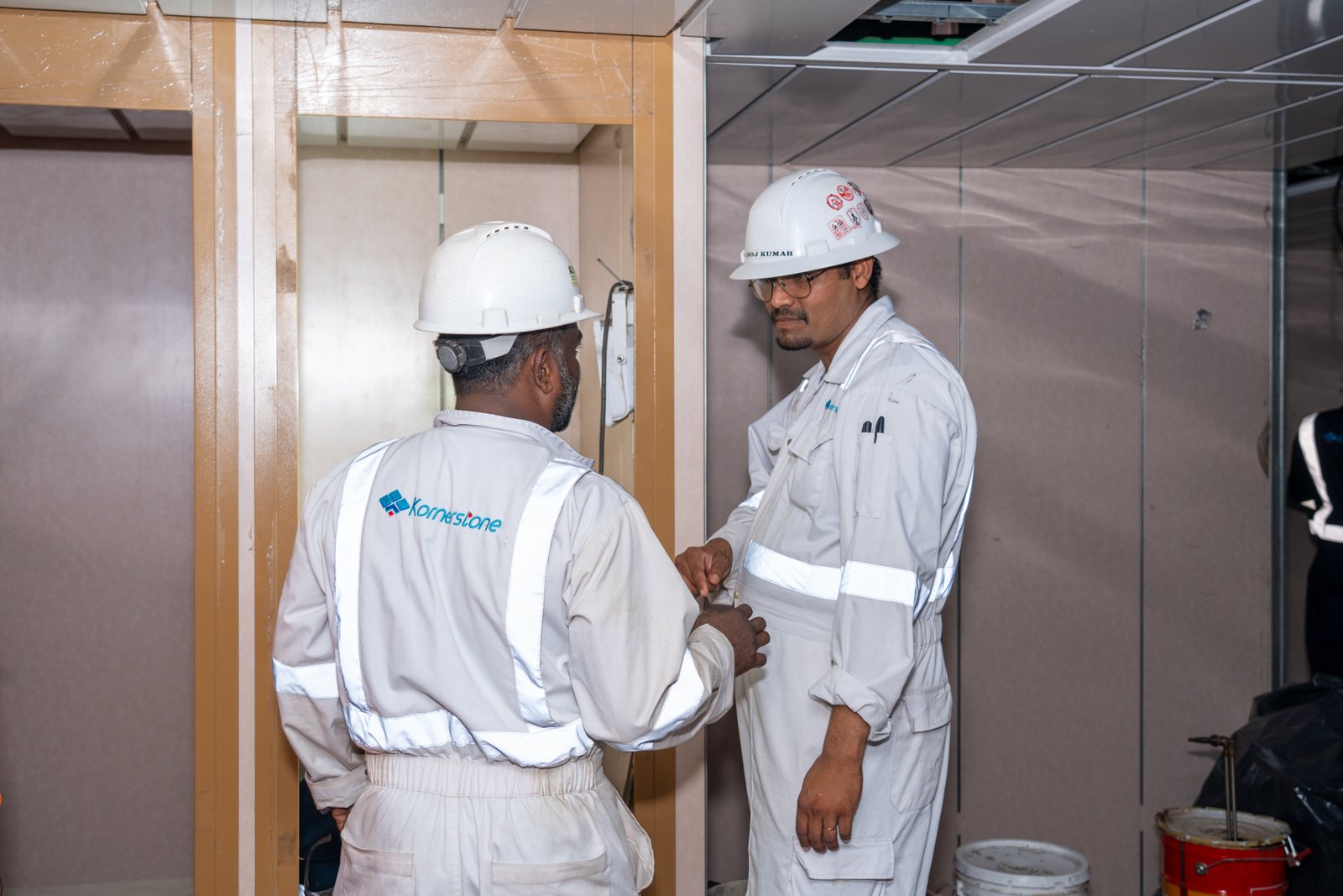 Two Kornerstone technicians in coveralls and hard hats shaking hands on site